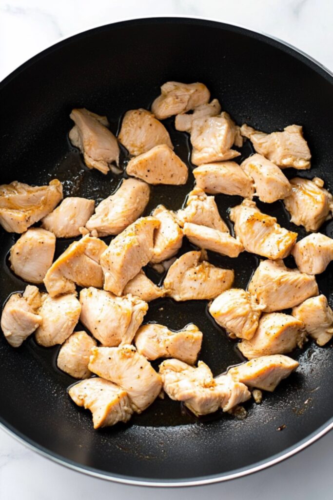 Diced boneless, skinless chicken pieces cooking in a non-stick pan, lightly browned and seasoned for a delicious low FODMAP sesame chicken dish.