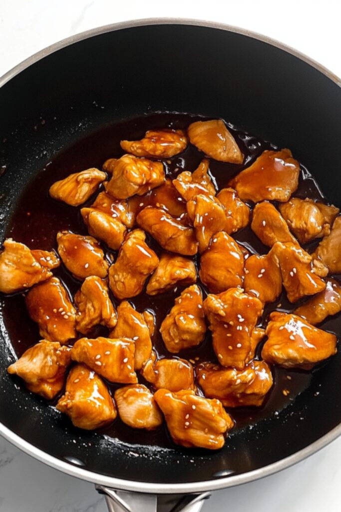 Juicy chicken pieces coated in a thick, shiny sesame sauce in a skillet, ready to be served over rice.