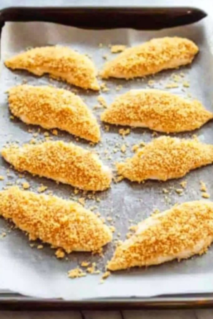 Dip a chicken tender into the egg mixture, then dip it in the dry ingredients and transfer to the baking sheet image