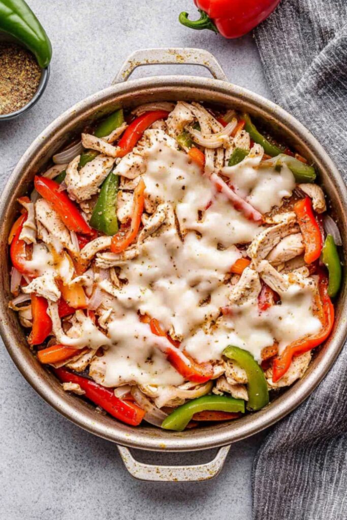 A close-up of a skillet filled with sautéed chicken, bell peppers, onions, and melted cheese, seasoned to perfection.