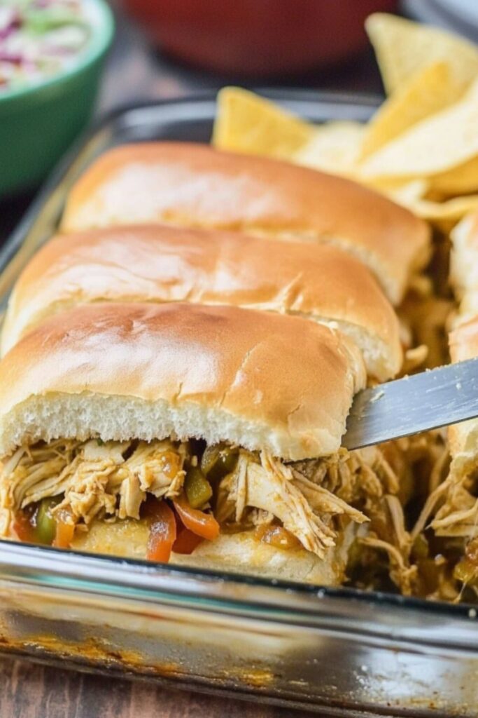 Hot chicken fajita sliders filled with seasoned shredded chicken and peppers being served from a glass baking dish