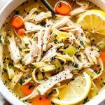 A close-up of a bowl of diabetic-friendly chicken noodle soup with shredded chicken, low-carb noodles, carrots, celery, and fresh parsley, garnished with a lemon wedge.