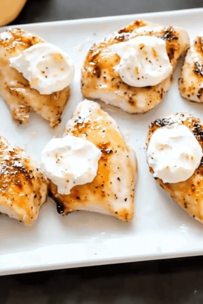 Seared chicken breasts served on a white plate topped with creamy goat cheese dollops