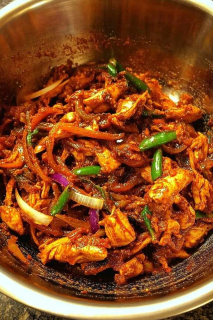 Bowl of spicy Nepali Chicken Choila garnished with sliced onions and green chilies