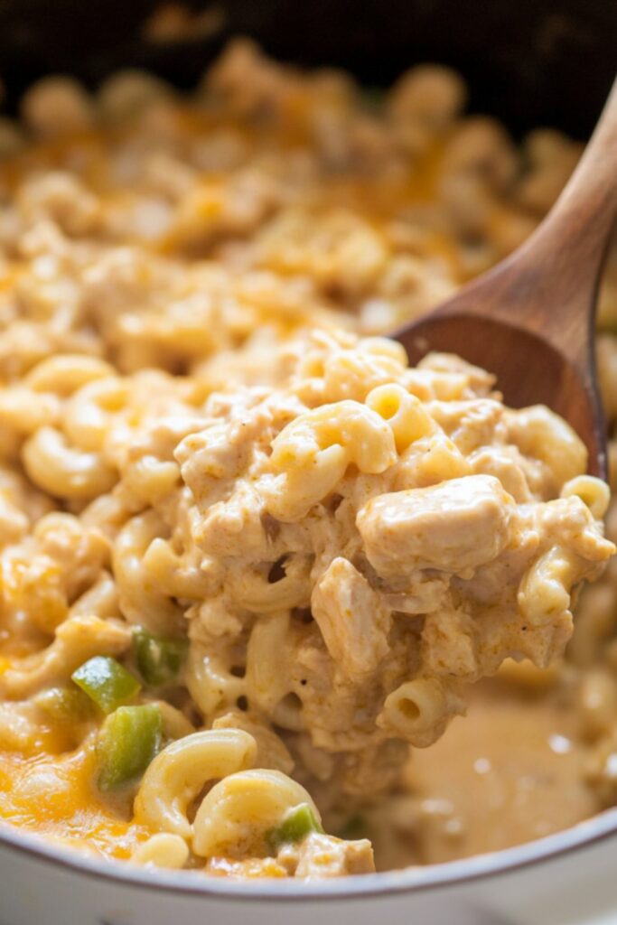 A wooden spoon scooping a serving of creamy chicken macaroni casserole with melted cheddar cheese.