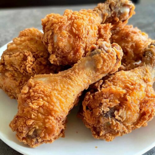A plate of golden, crispy homemade KFC-style fried chicken drumsticks with a crunchy coating.