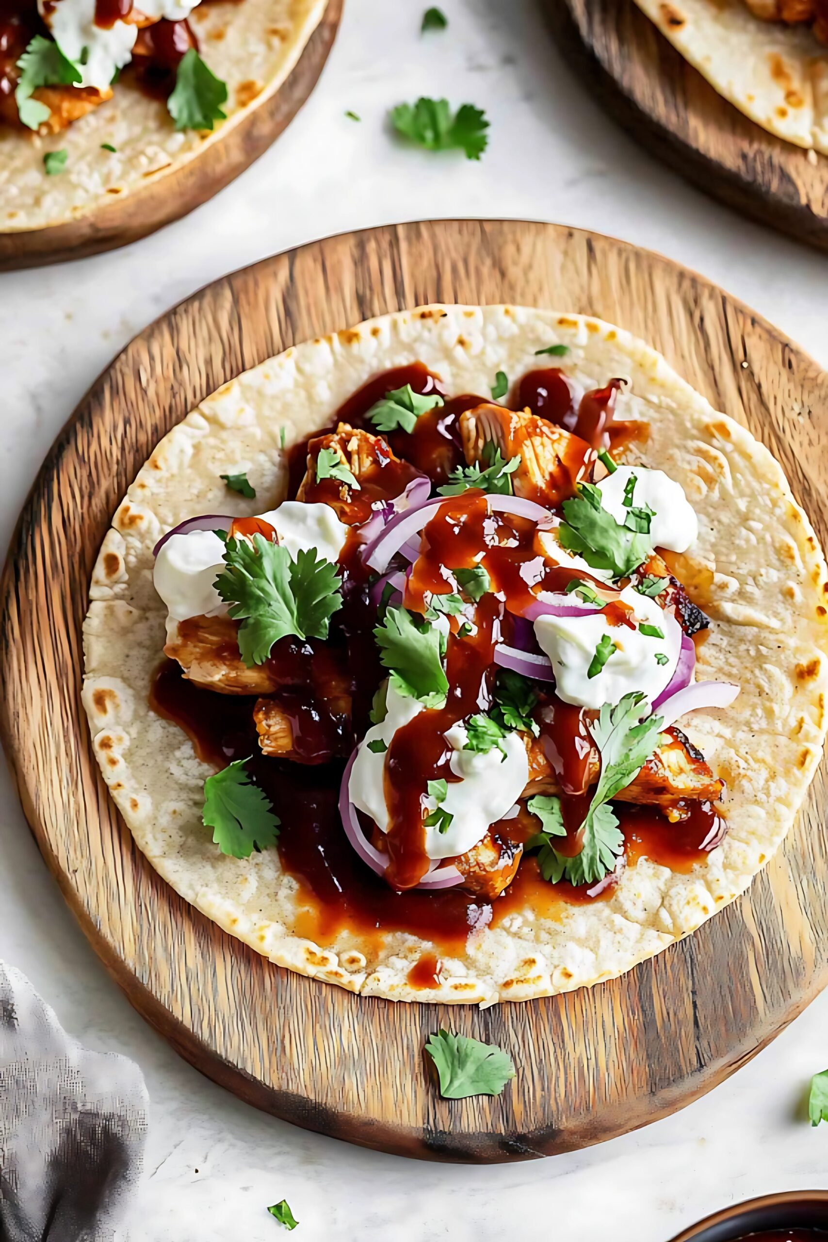 A tortilla wrap filled with BBQ chicken, creamy cheese, red onions, and cilantro, drizzled with extra BBQ sauce.