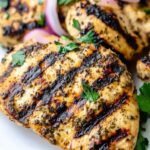 Close-up of grilled chicken breast with charred grill marks, marinated in a flavorful low-salt herb and garlic blend, garnished with fresh parsley and red onion slices.