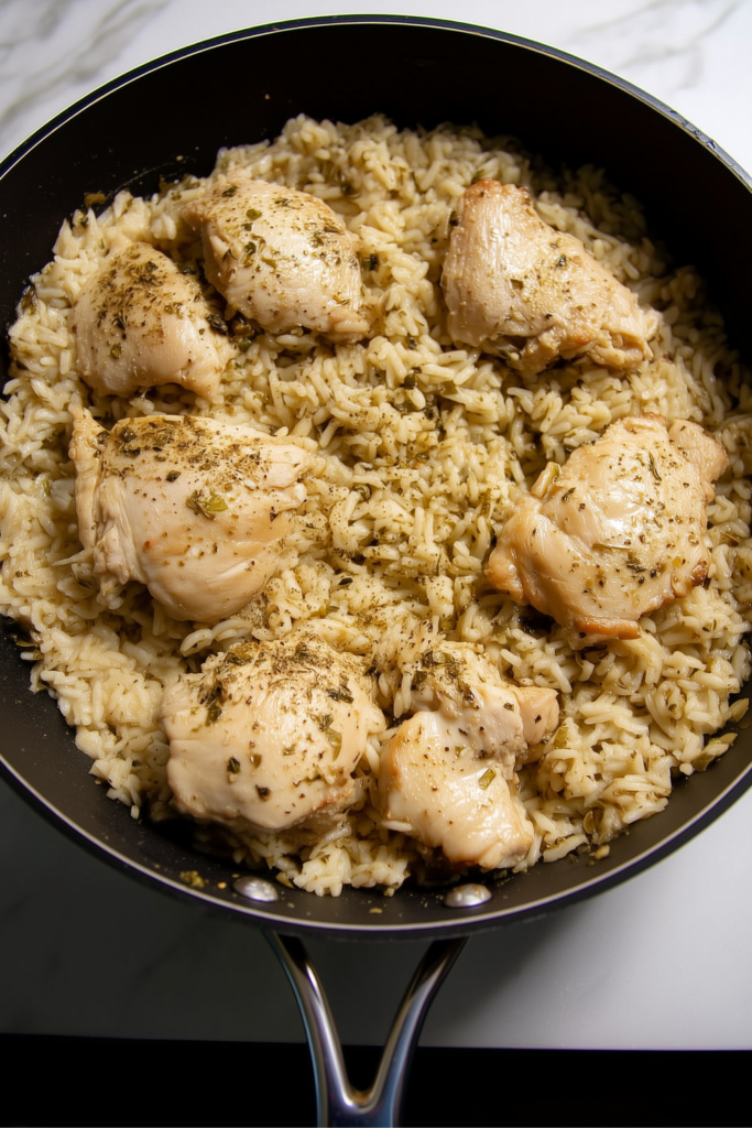 Fully cooked lemon chicken and rice in a black skillet, seasoned with herbs