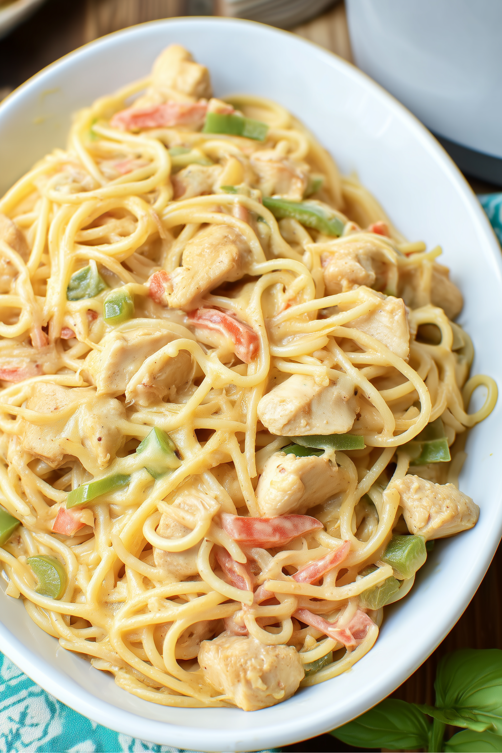 Close-up of low sodium chicken spaghetti with chunks of chicken breast, red and green bell peppers, and creamy sauce in a white serving bowl.