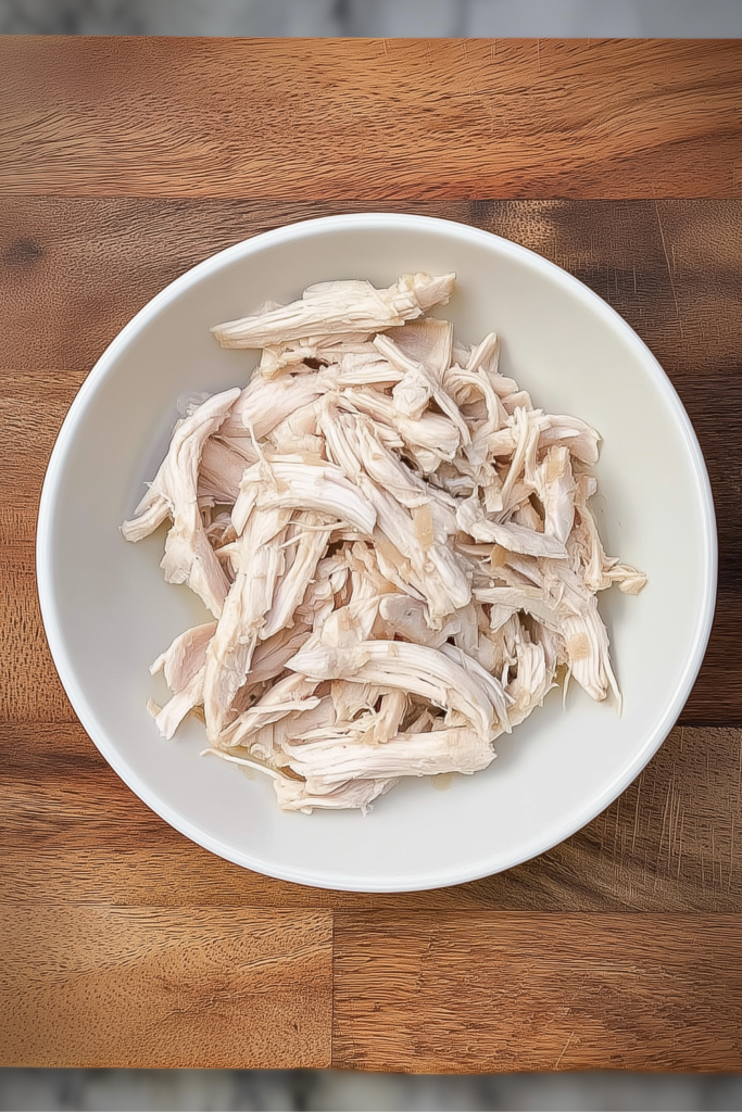 Bowl of freshly shredded boiled chicken breast on a wooden surface