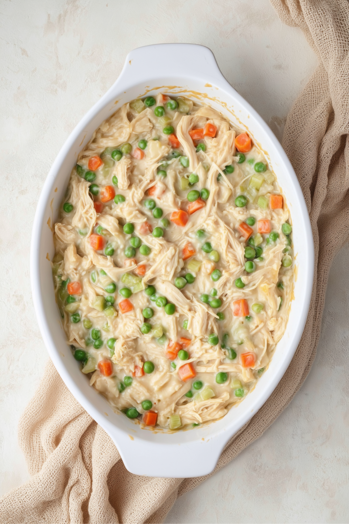 Unbaked dairy-free chicken pot pie filling with peas, carrots, and shredded chicken in a white baking dish