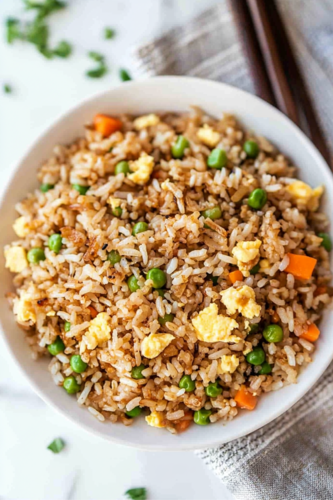 Top view of hibachi chicken fried rice in a white bowl with peas, carrots, and egg on a marble background