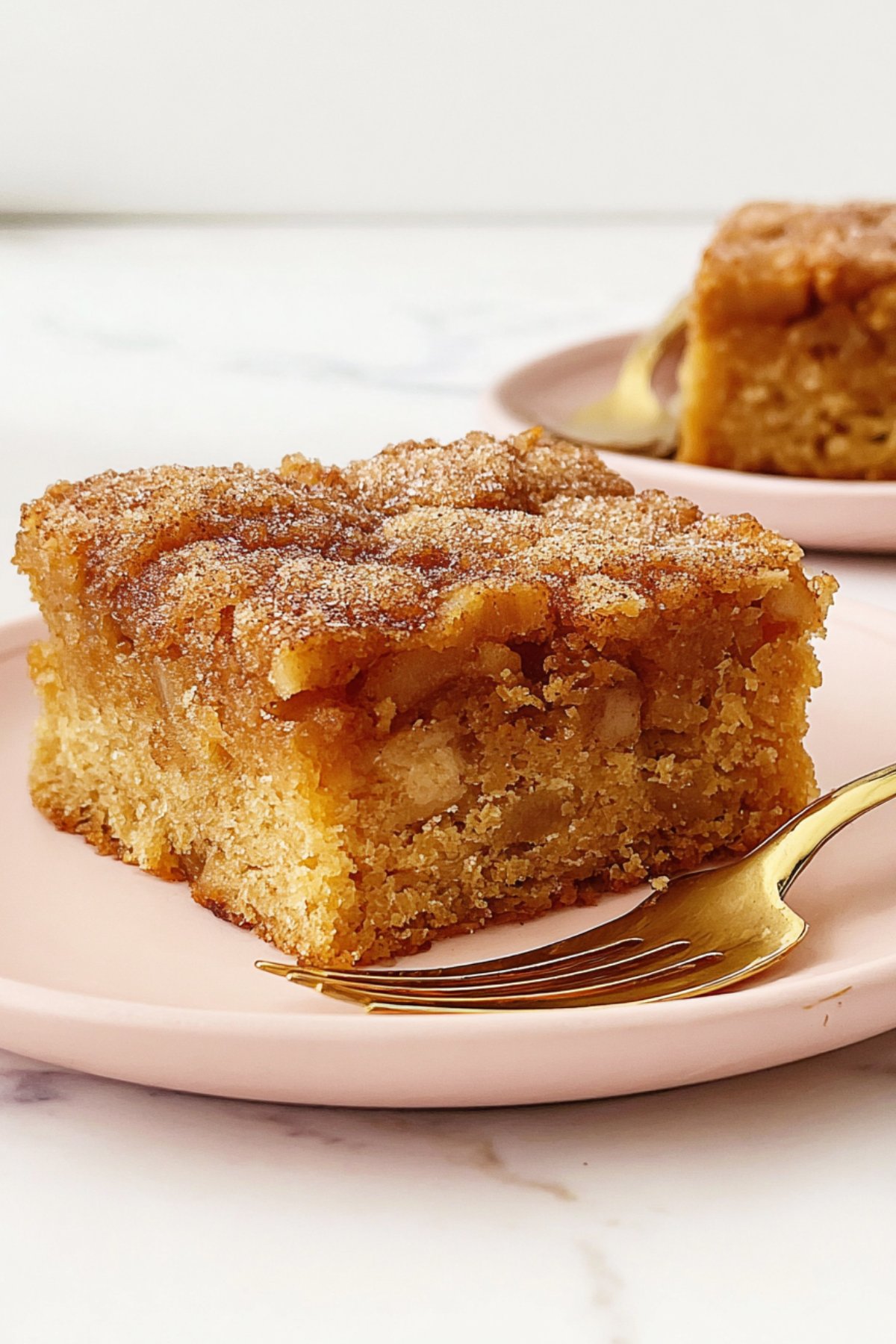 Moist apple snack cake slice with a cinnamon sugar topping, styled on a light pink plate.