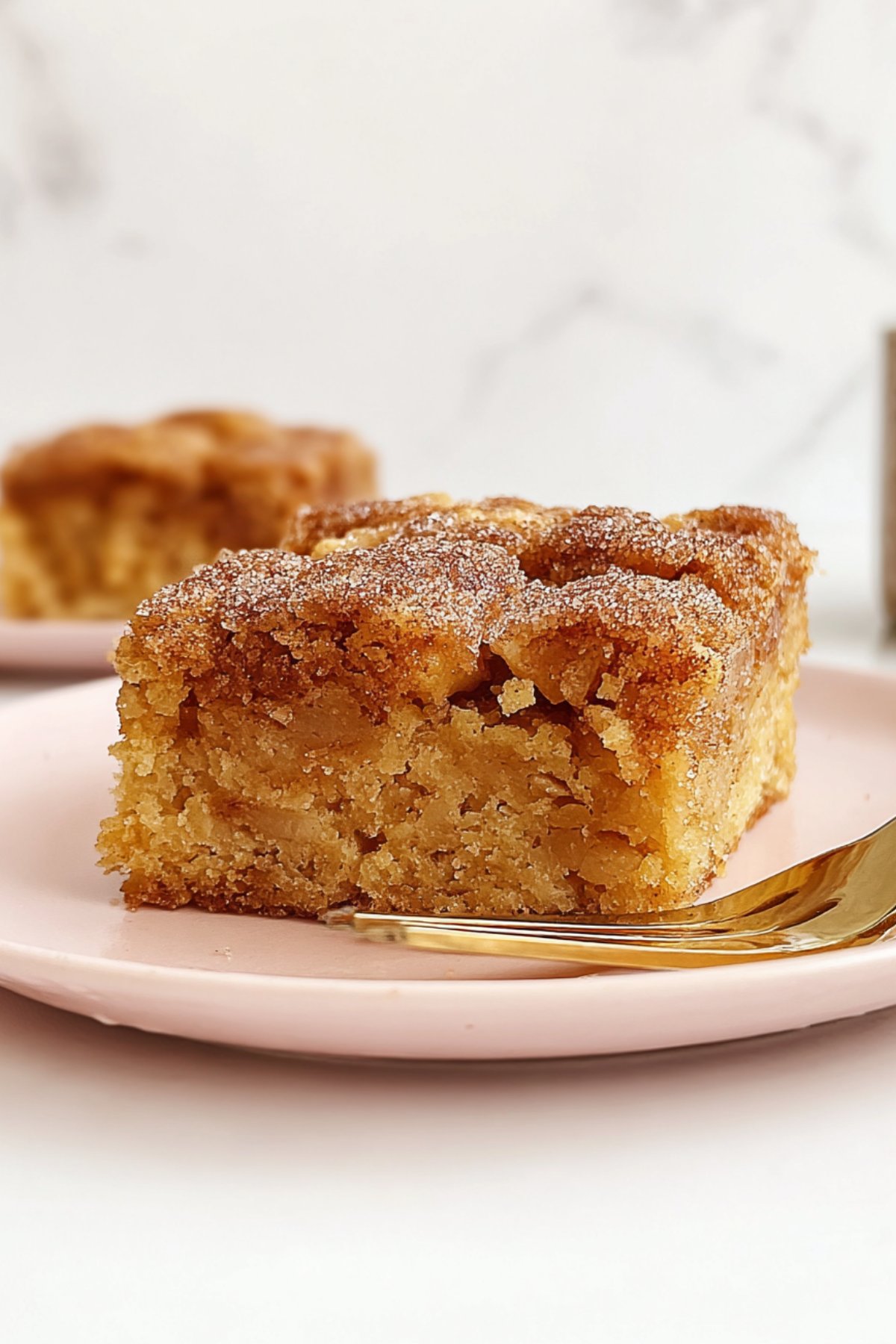 Golden apple snack cake slice on a fork-ready pink plate, topped with cinnamon sugar.