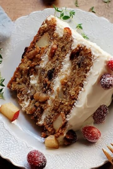 Festive slice of spiced apple and cranberry Thanksgiving layer cake served on a glass plate with a gold fork.