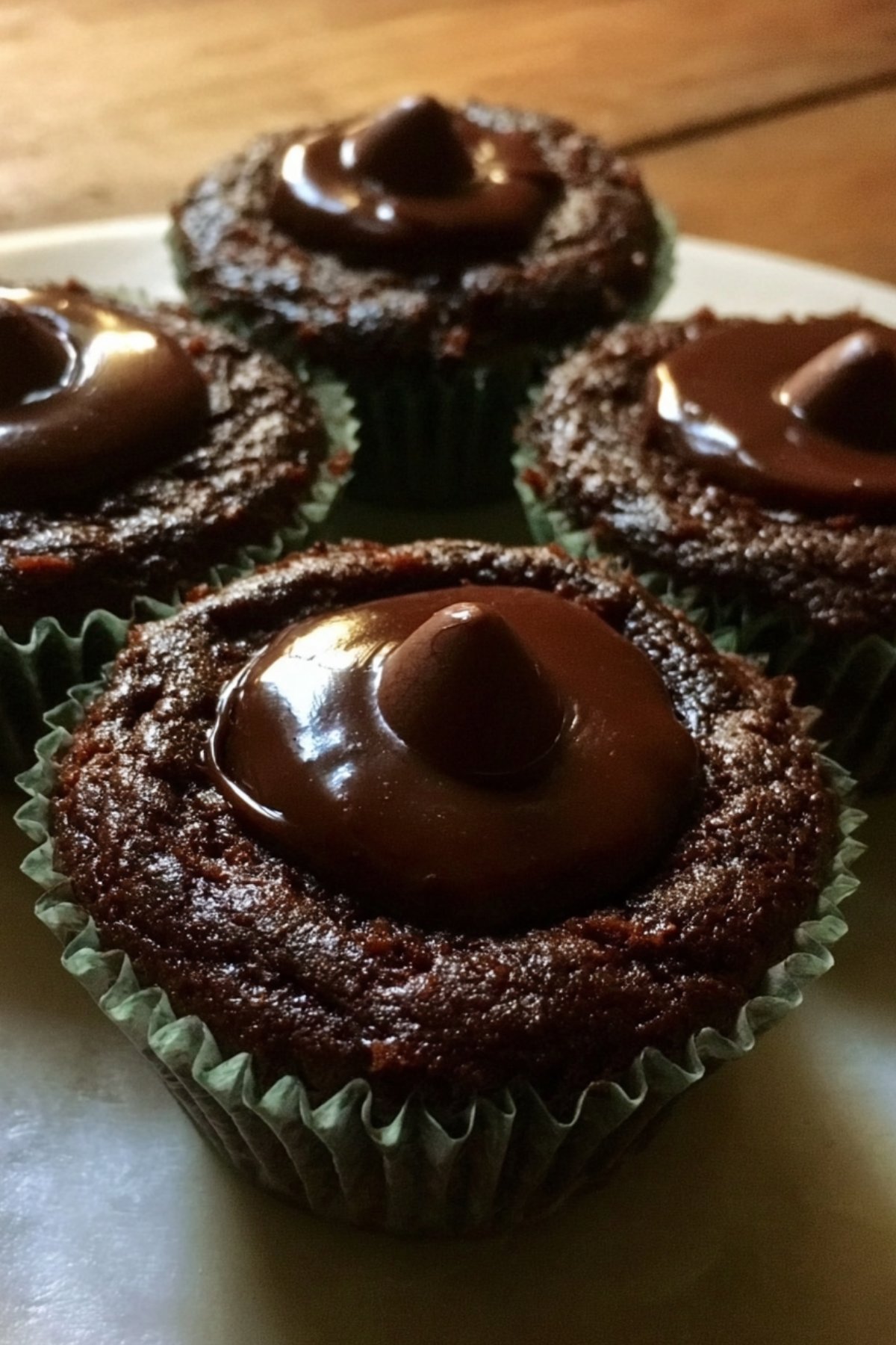 Chocolate torte cupcake with a glossy chocolate topping in focus, with more cupcakes in background.