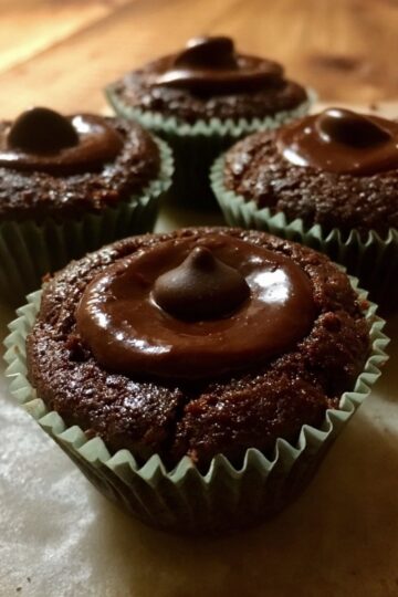 Close-up of chocolate torte cupcake topped with glossy chocolate frosting and a Hershey’s Kiss-style garnish.