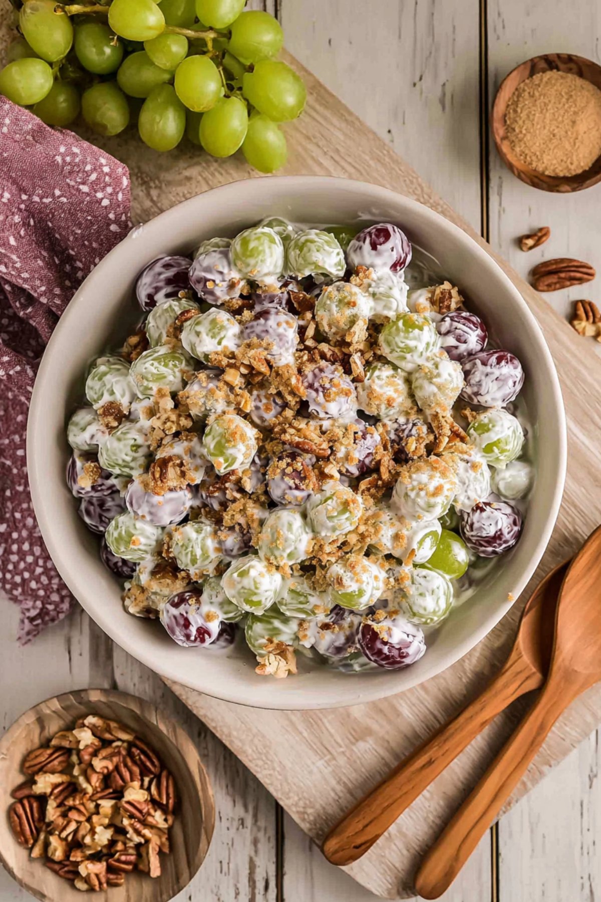 Close-up of grape salad in a white bowl topped with pecans and brown sugar.