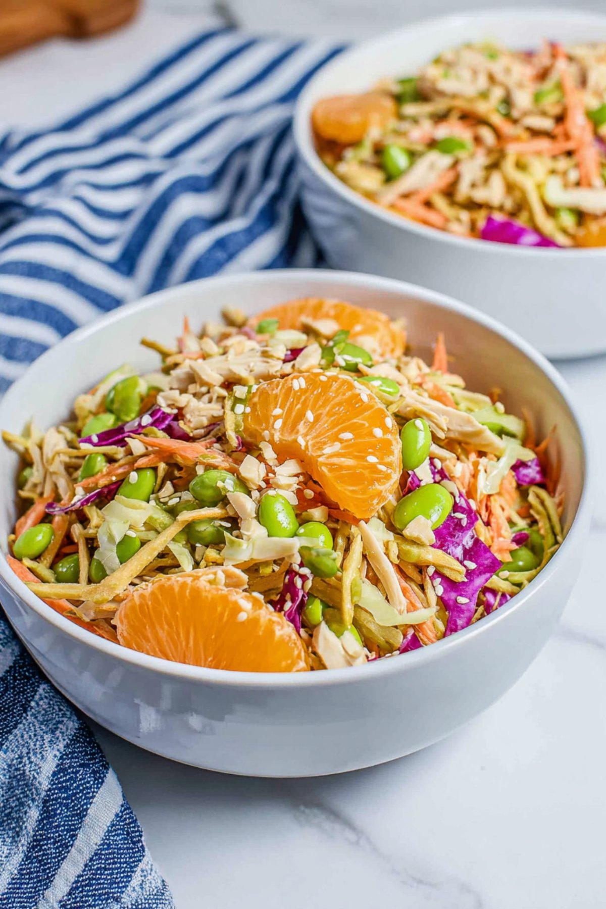 Bowl of Chinese chicken salad garnished with mandarin slices, sesame seeds, and crunchy noodles.