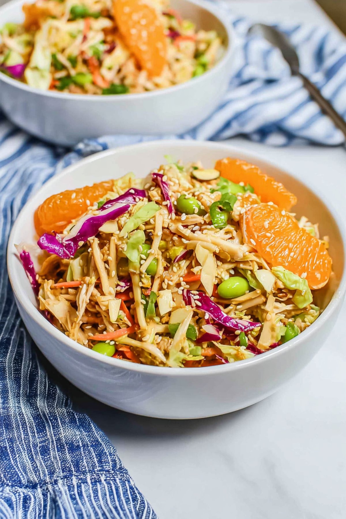 Chinese chicken salad in a white bowl with mandarins, edamame, shredded carrots, and sesame seeds.