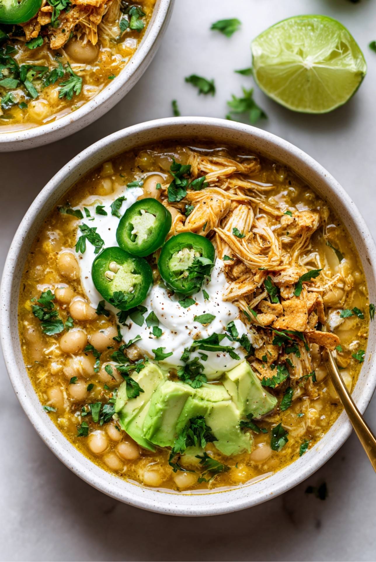 Two bowls of creamy white bean chicken chili with shredded chicken, lime, and fresh cilantro.