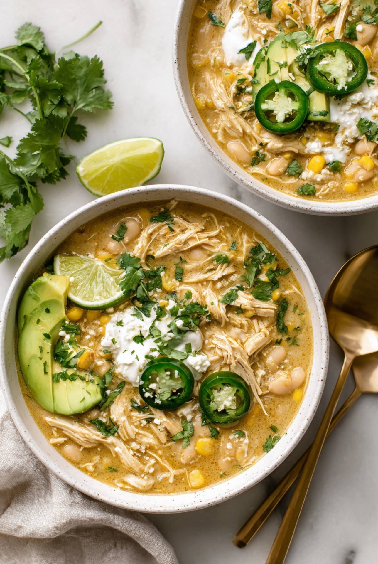 Bowl of creamy white chicken chili with corn, avocado, jalapeños, and cilantro garnish.