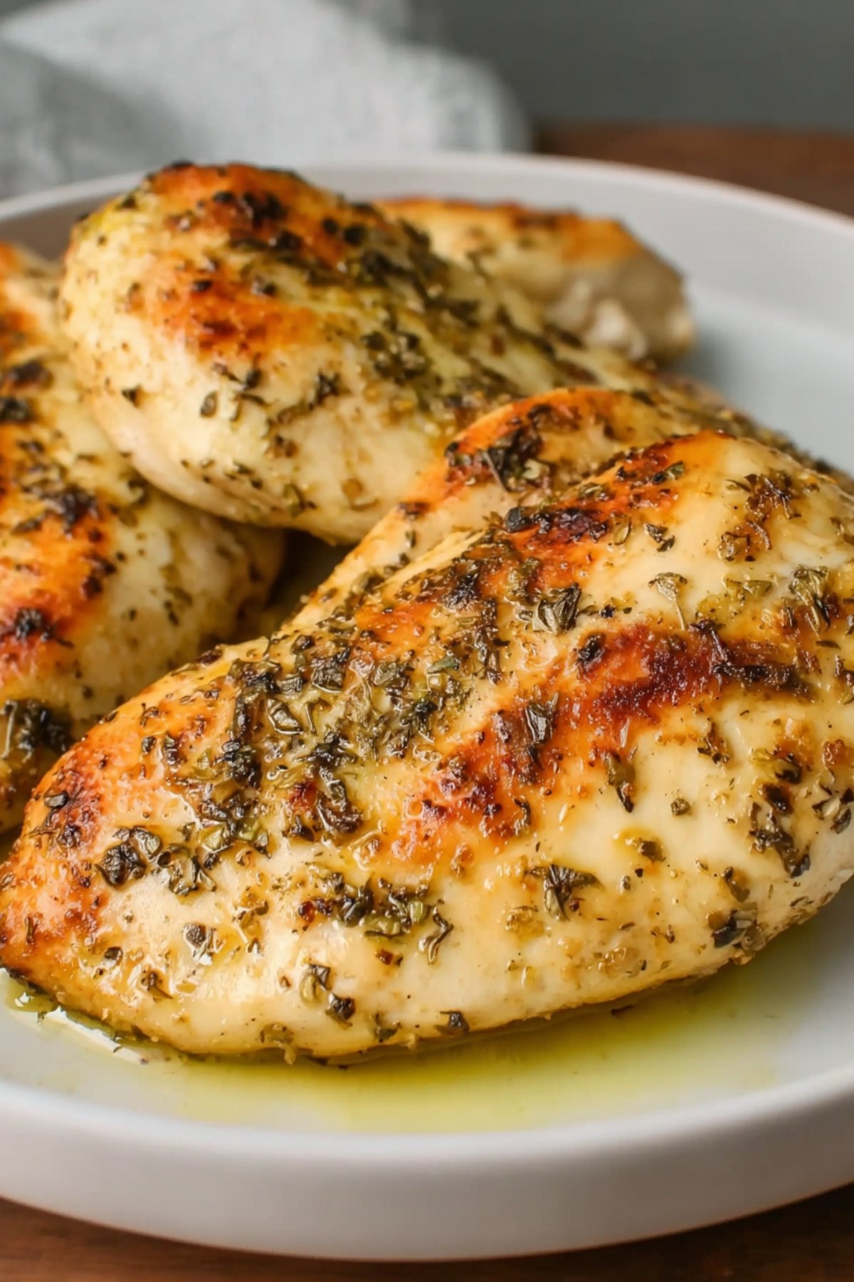 Juicy seasoned chicken breast cooked in olive oil and herbs on a dinner plate.