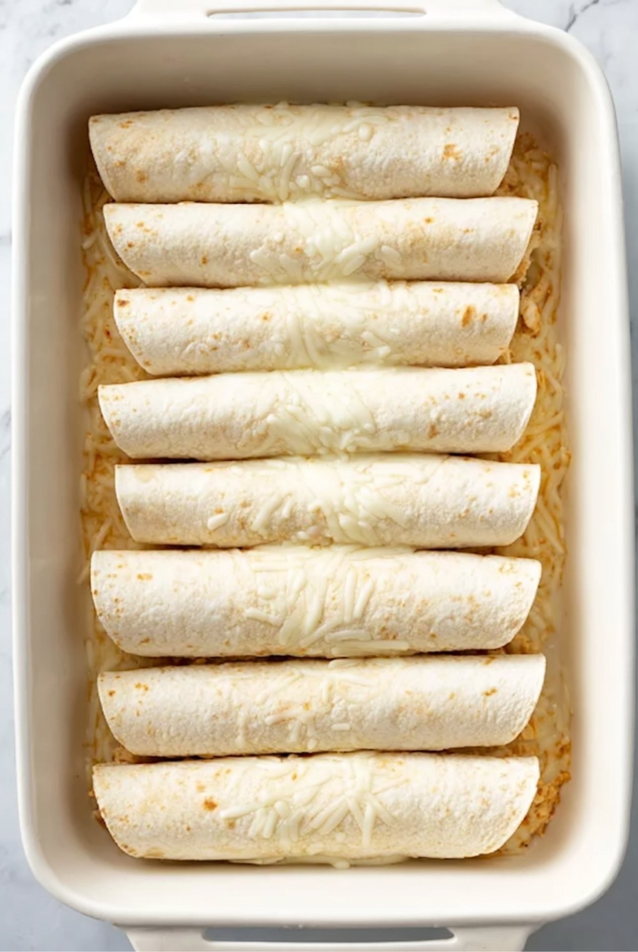 Unbaked rolled tortillas filled with chicken placed in a casserole dish, ready for White Chicken Chili Enchiladas.