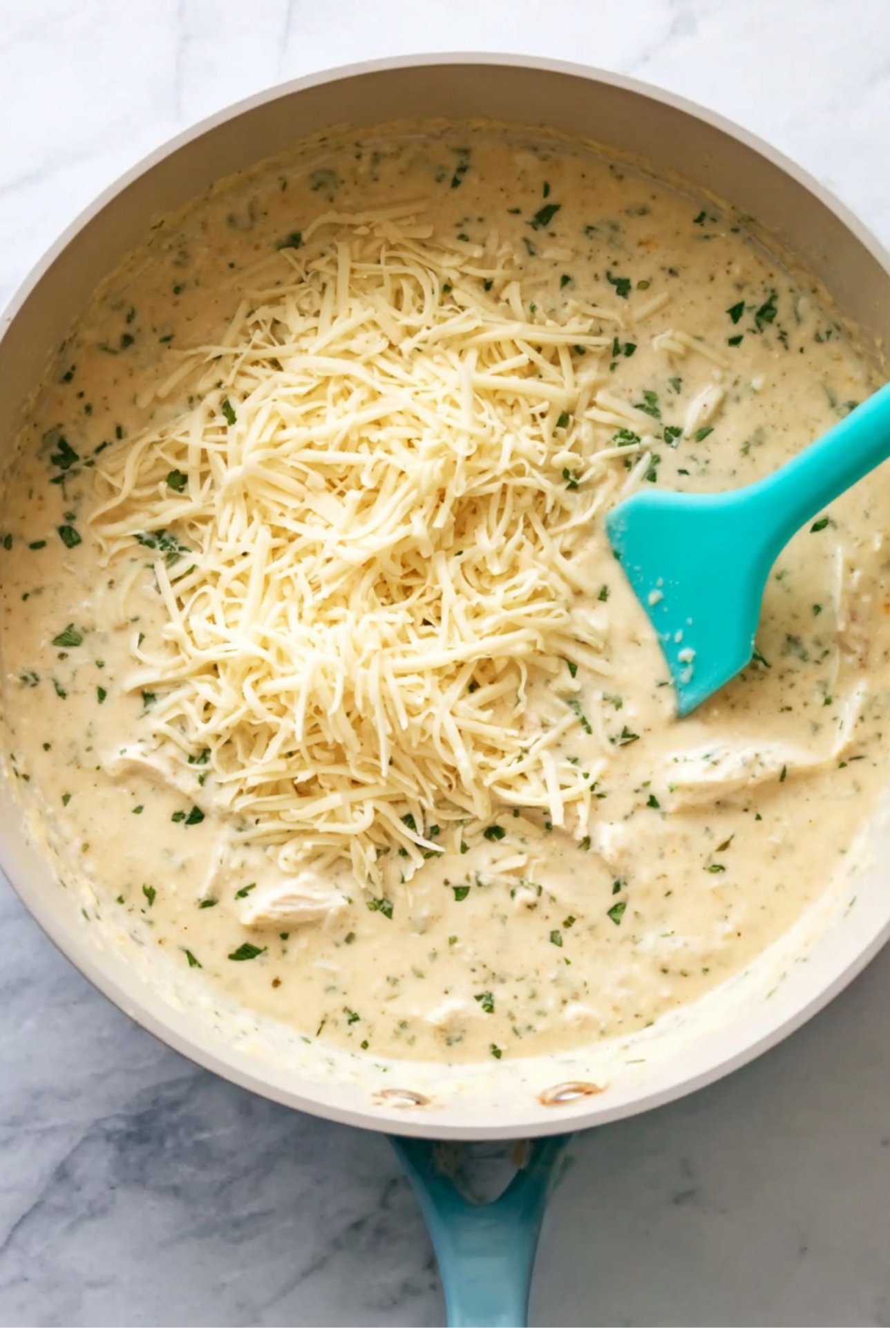 Pan of creamy sauce with shredded cheese and herbs being stirred with a spatula for White Chicken Chili Enchiladas.