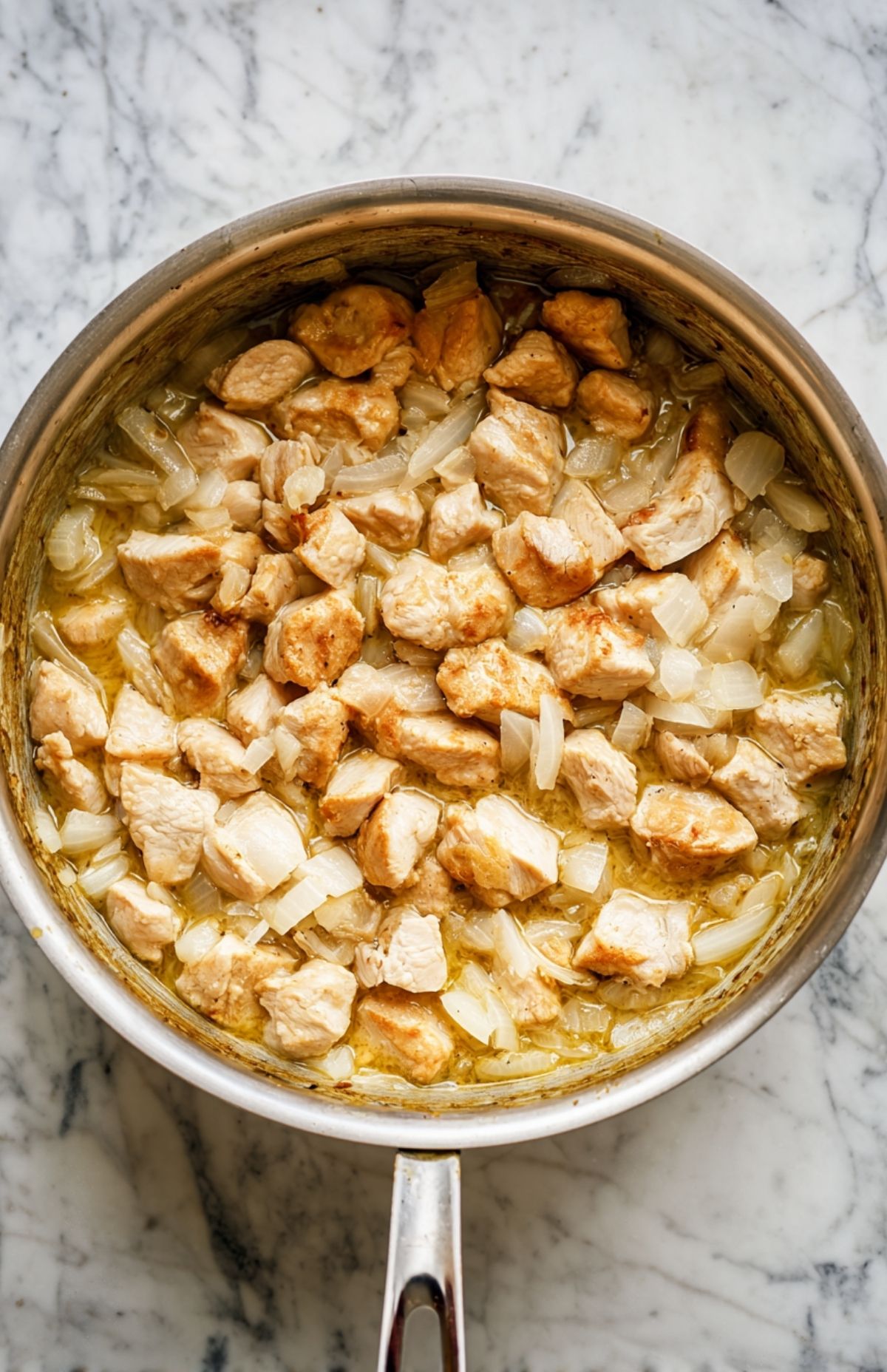 Chicken and onions sautéing in a skillet as the first step in making creamy white bean chicken chili.