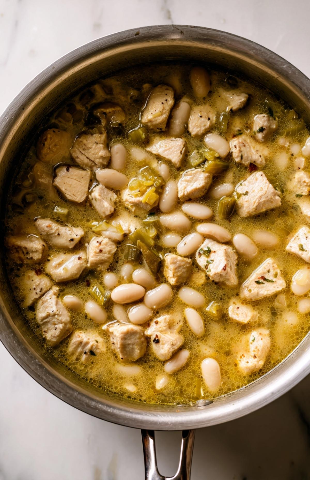 Pot of chicken, beans, and broth simmering together for creamy white bean chicken chili.