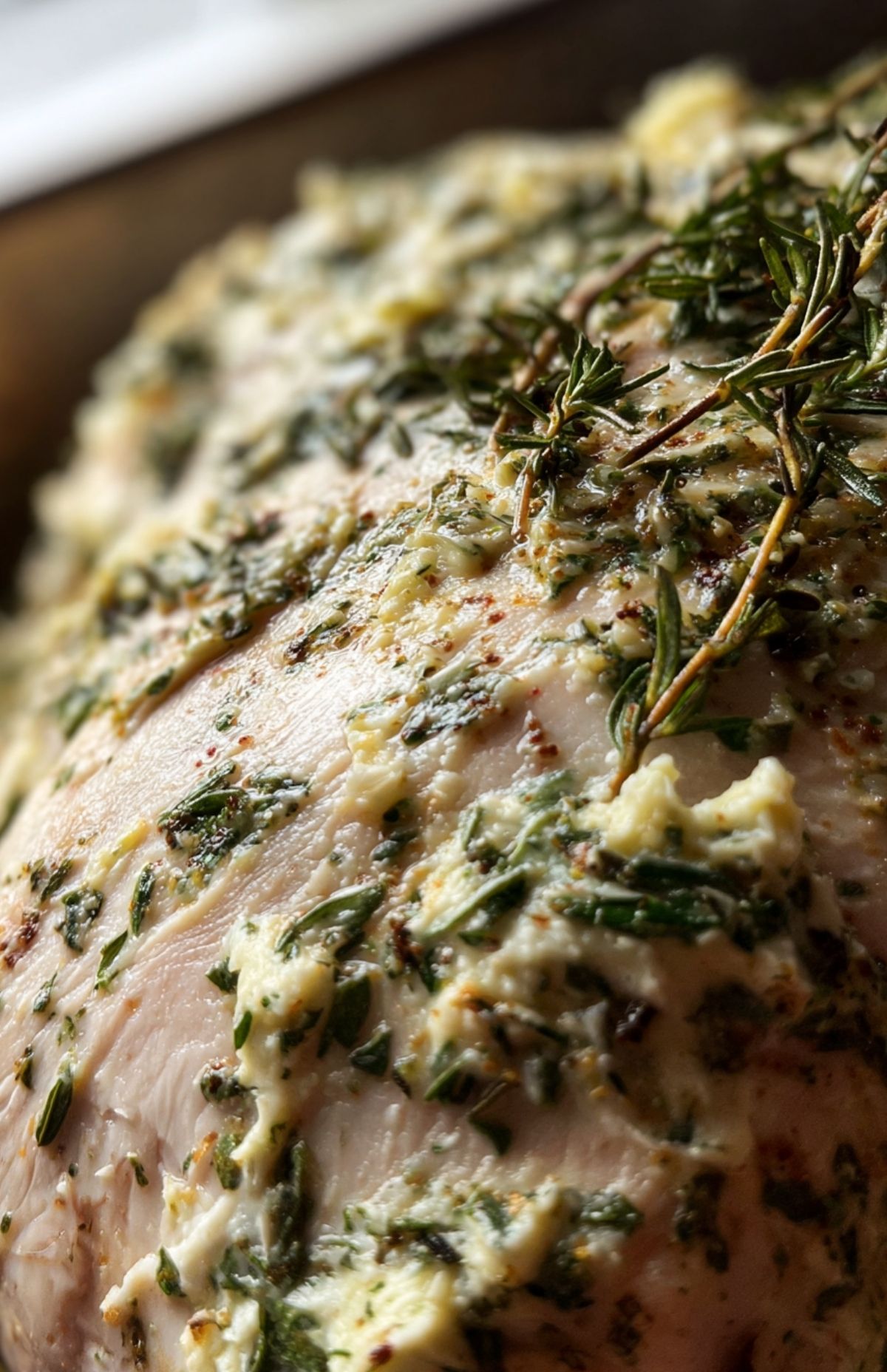 Uncooked turkey breast coated with garlic herb butter and fresh rosemary.