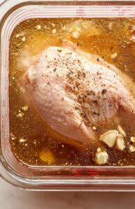 Glass bowl of golden brine with minced garlic and black pepper floating on top.