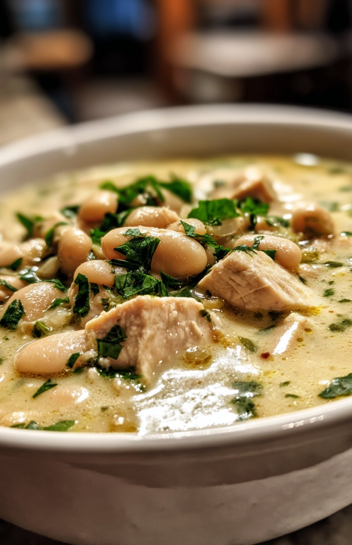 Bowl of creamy white bean chicken chili topped with parsley, showing beans and juicy chicken chunks.