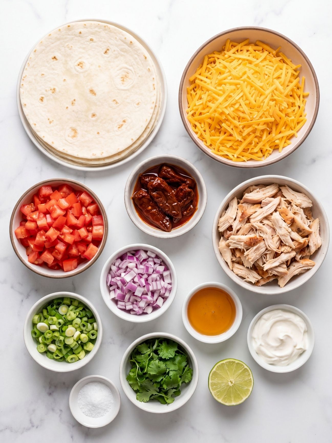 Fresh ingredients for chipotle chicken quesadillas including shredded chicken, cheese, tortillas, chipotle peppers, and honey.
