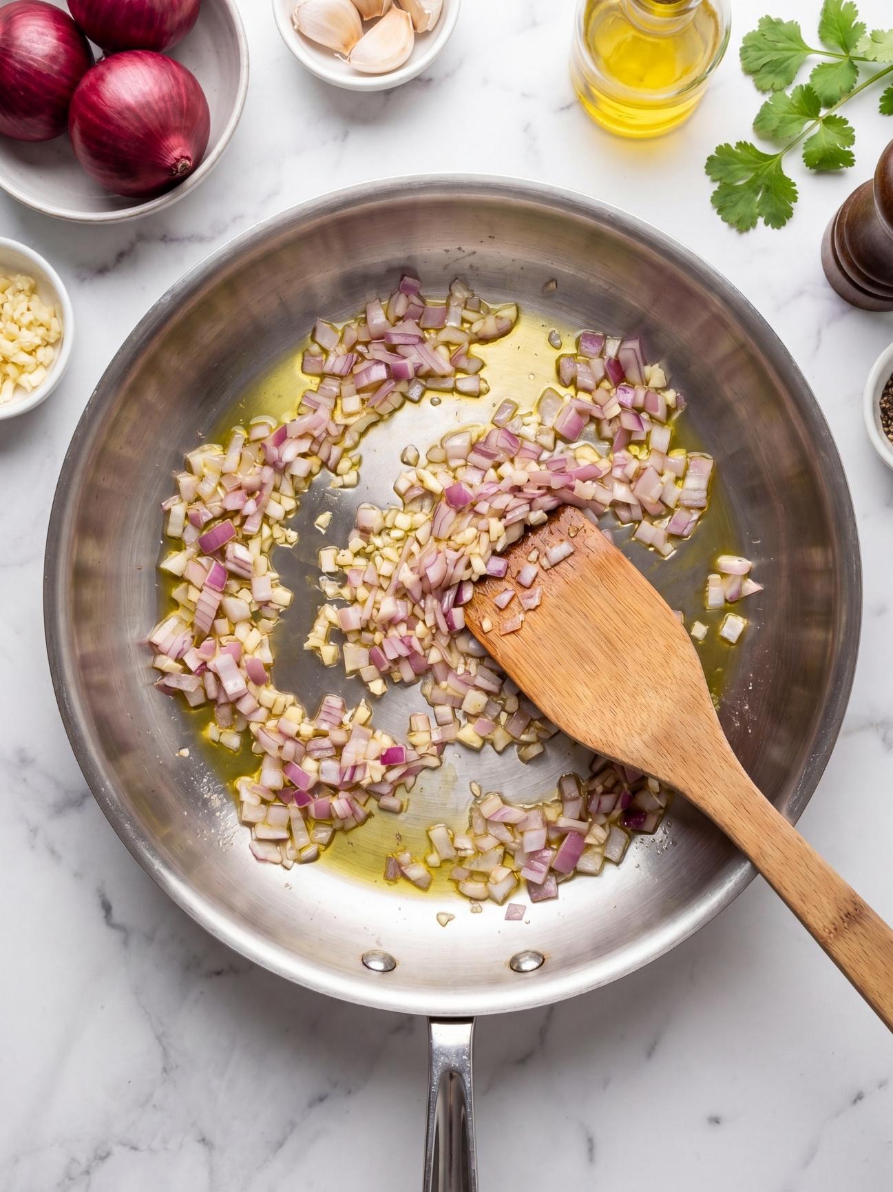 Sautéing chopped red onions and garlic in a stainless steel skillet for chipotle chicken quesadilla filling.