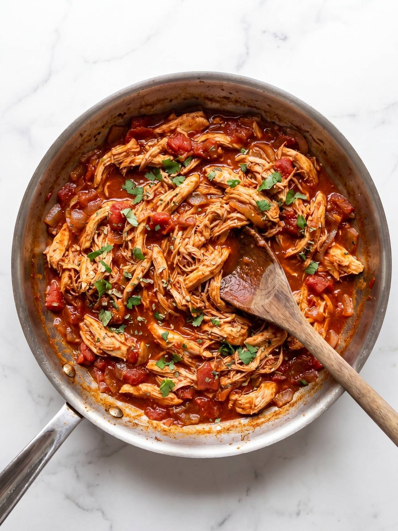 Shredded chicken mixed into a spicy chipotle tomato sauce with fresh cilantro in a skillet.