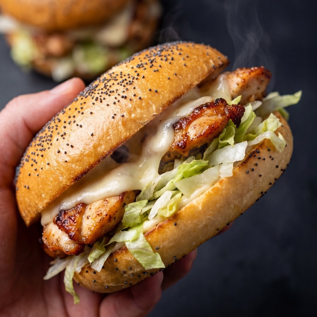A hand holding a toasted poppy seed bun filled with grilled chicken, melted cheese, and shredded lettuce.