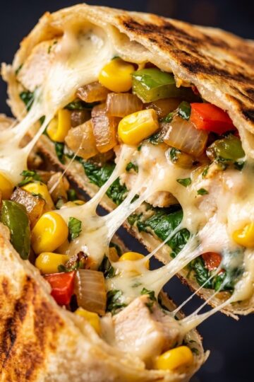 A close up view of a chicken burrito sliced in half with melted cheese stretching between the two pieces.