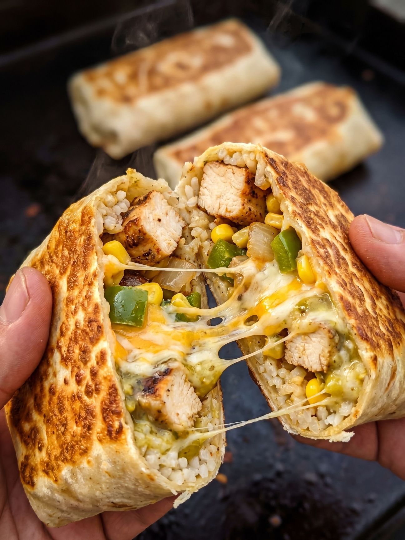 Two hands holding a grilled chicken burrito sliced in half with a cheesy pull, showing rice, chicken, corn, and peppers inside.