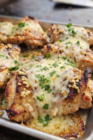 Close-up of crispy griddle-cooked chicken parmesan topped with melted mozzarella, marinara sauce, and fresh parsley on a baking sheet.