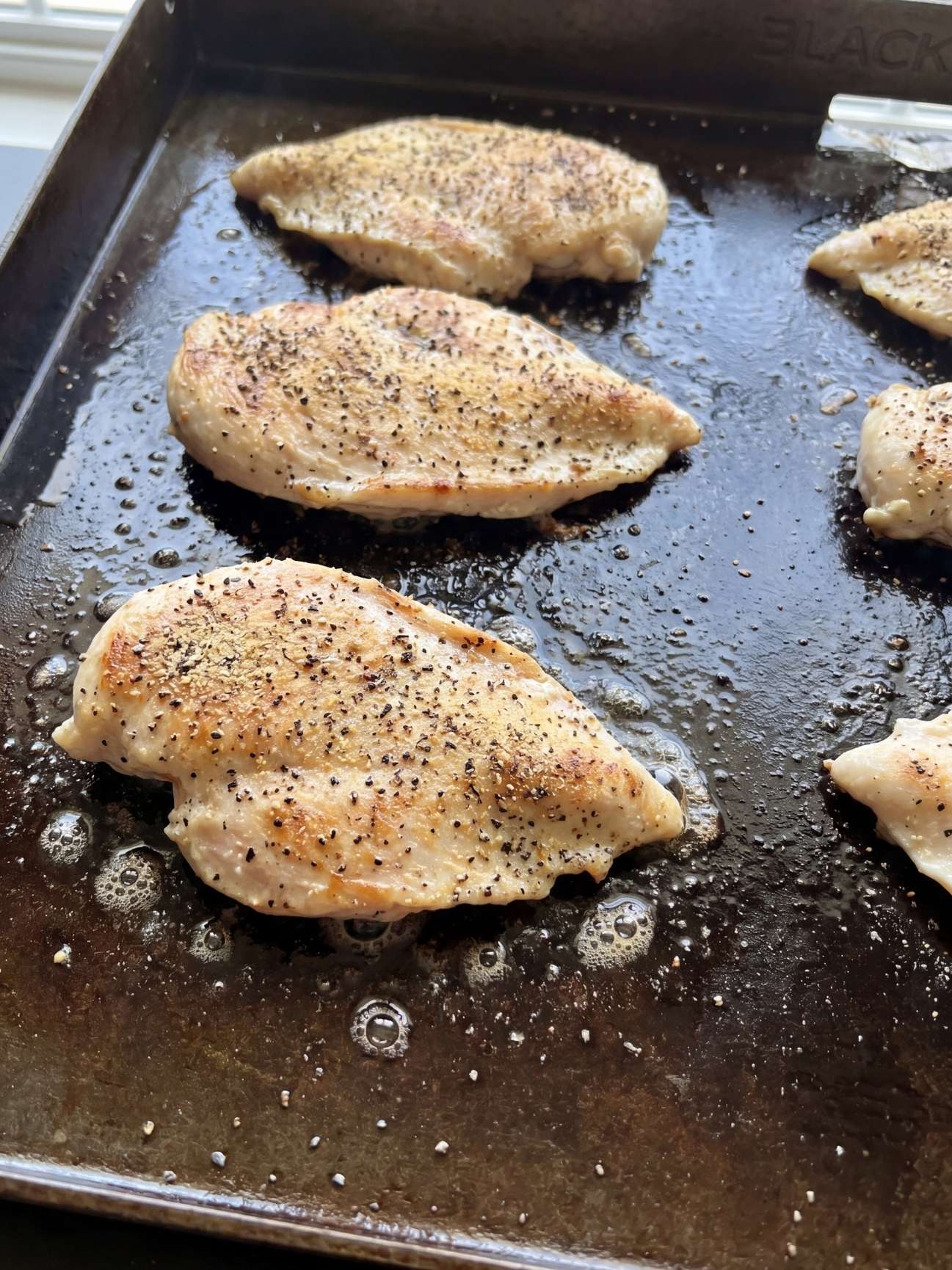 Seasoned chicken breasts searing and sizzling on a hot Blackstone griddle.