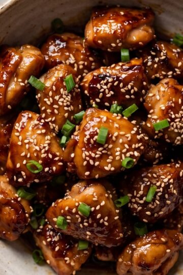 Close-up of crispy Blackstone orange chicken bites topped with sesame seeds and fresh green onions in a ceramic bowl.
