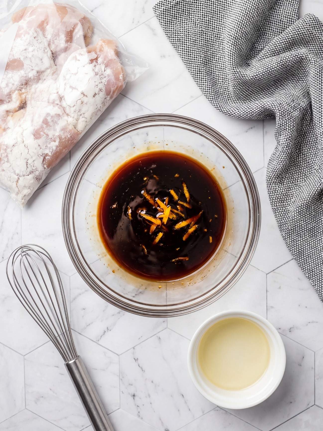 Whisking together a homemade orange sauce with fresh juice, soy sauce, brown sugar, garlic, and ginger in a glass bowl.