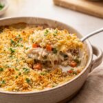 Creamy chicken and vegetable rice bake topped with golden brown panko breadcrumbs and fresh parsley being scooped out of a ceramic dish with a large spoon
