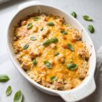 A creamy and bubbly chicken and rice casserole baked to golden perfection in an oval white ceramic dish garnished with fresh basil leaves