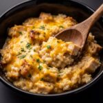 Creamy chicken and brown rice casserole topped with melted cheddar cheese and fresh parsley served in a black bowl with a wooden spoon